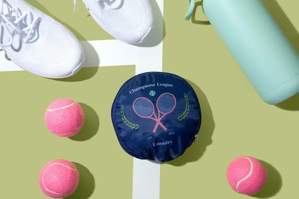 Miamica's Tennis collection laundry bag features a round, navy blue bag with a pink tennis racket motif design.