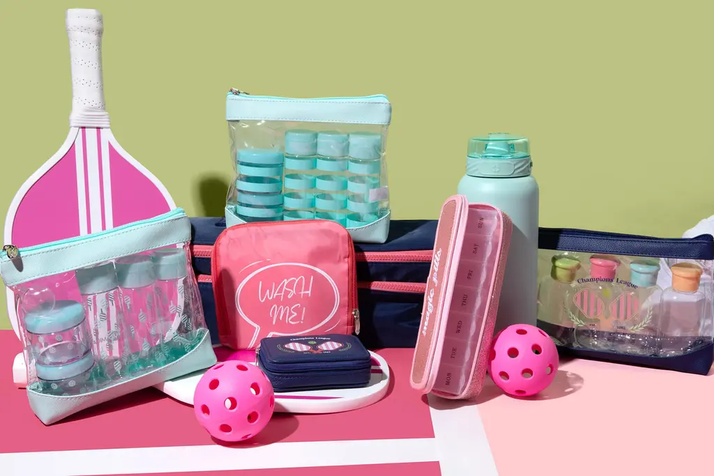 Miamica's Pickleball collection accessories are displayed on a pink court. They feature Cool Court Blue Bottle Sets, a pink "Wash Me" Laundry Bag, and navy blue and pink pill cases.